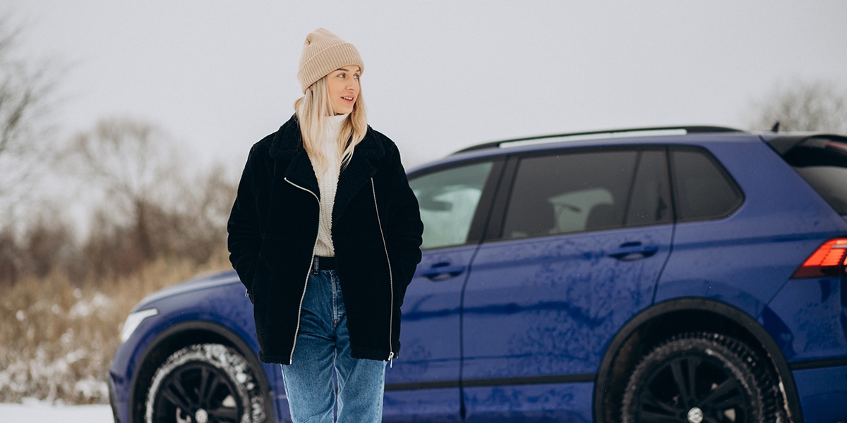 Woman in winter clothes standing by her car